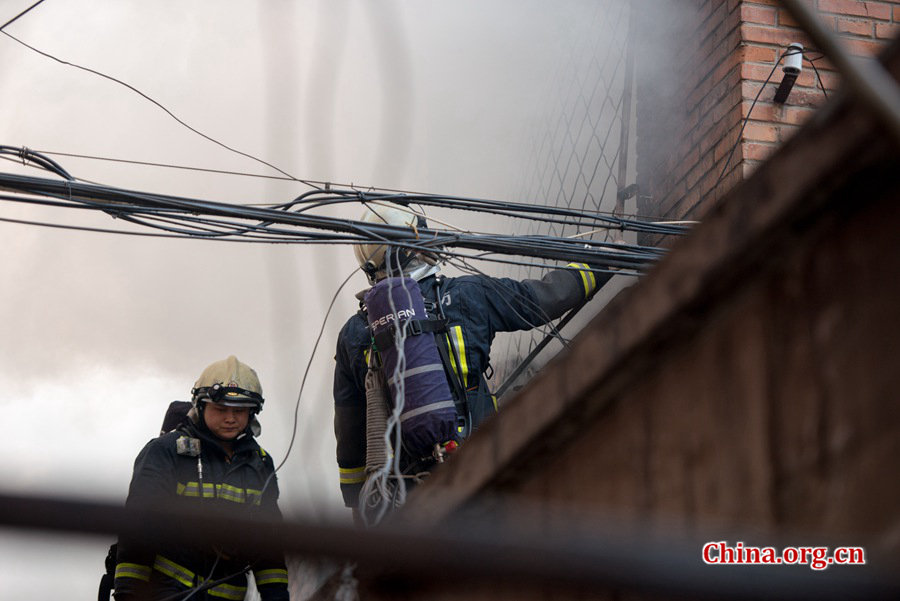 Firefighters pump water into a blazing building in a residential area in downtown Beijing on Thursday, March 5, the traditional Chinese Lantern Festival. The building located between Linglong Rd. and Qixiancun Rd. in Haidian District, is used as a warehouse of Gehua, Beijing&apos;s local cable TV service provider. The burning rubber from the cable wire gives out a strong black smoke. [Photo by Chen Boyuan / China.org.cn]