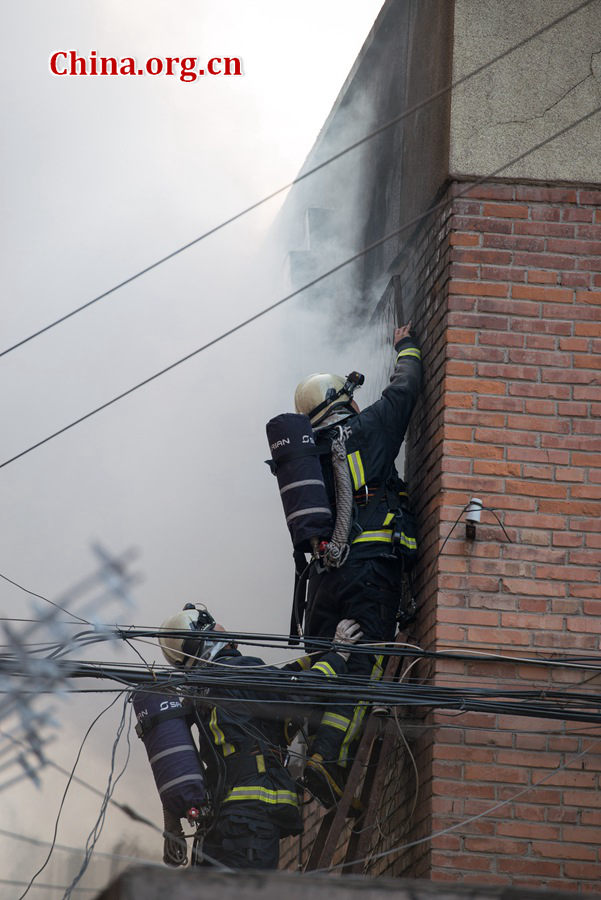 Firefighters try to break into a blazing building on Thursday, March 5, the traditional Chinese Lantern Festival. The building, according to people who live nearby, is used as a warehouse of Gehua, Beijing&apos;s local cable TV service provider, and the burning rubber from the cable gives out a strong black smoke. [Photo by Chen Boyuan / China.org.cn]