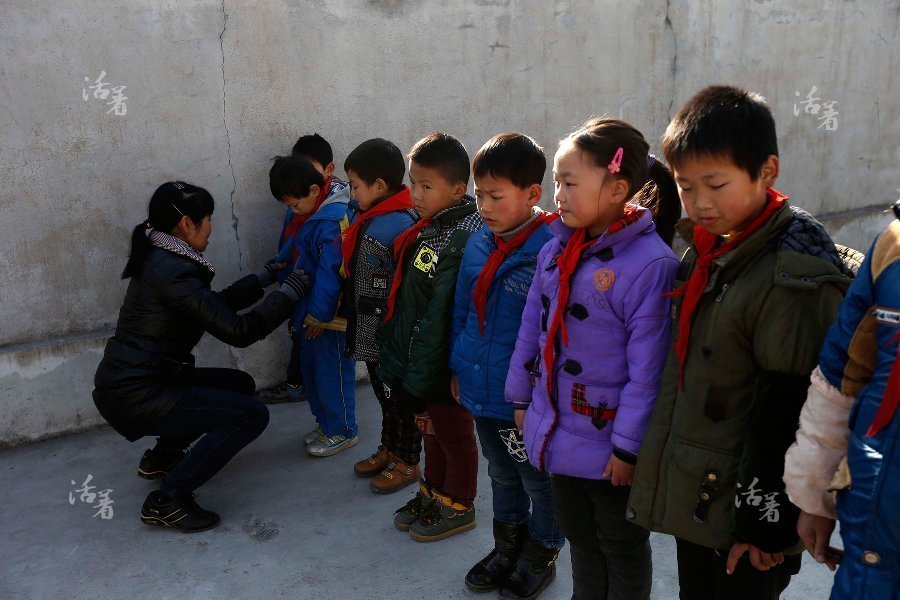 Teacher Liao Meixiang helps a student do up his buttons at Dalishan elementary school in Longyou County of Zhejiang province. [Photo/qq.com] 