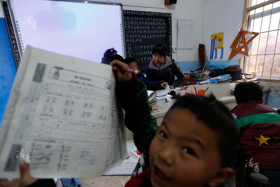 A student shows his exercise book to the photographer while Teacher Liao is busy tutoring other students in the classroom. [Photo/qq.com] 