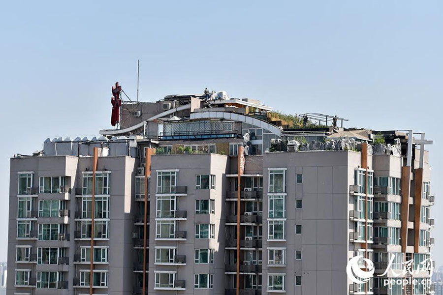 Two people are seen working on the roof of a 26-story building in downtown Beijing, April 22, 2015. The building came into the spotlight two years ago, when it was discovered that a luxury illegal villa was built on its roof by a top-floor resident. Zhang Biqing, the man who had the villa built, tore it down when confronted by local law enforcement. [Photo: people.cn]