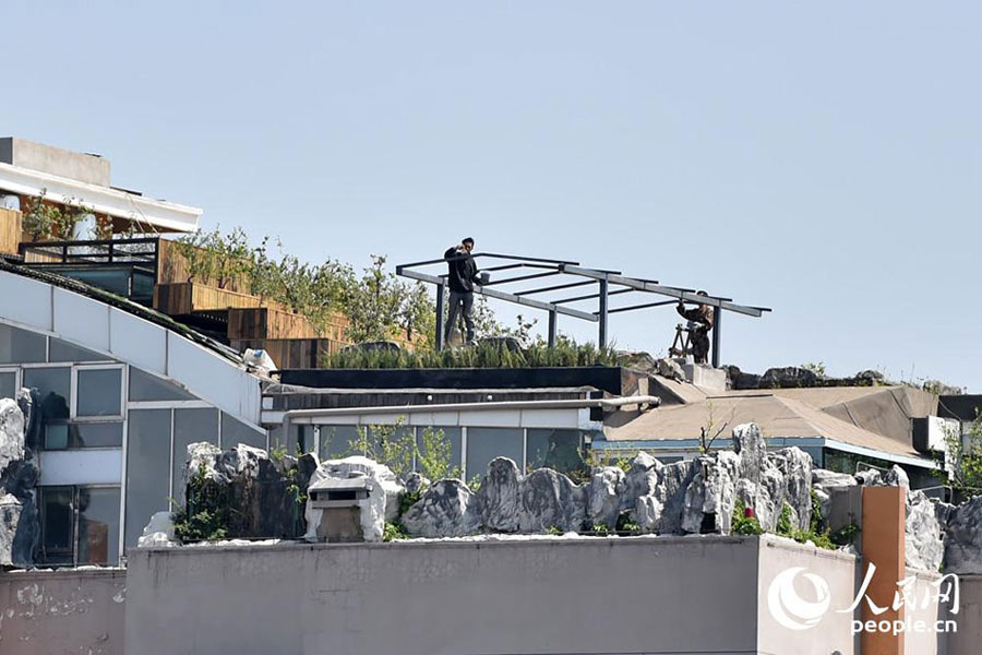 Some artificial rocks are seen sitting on the edge of the roof of a 26-story building in downtown Beijing, April 22, 2015. The building came into the spotlight two years ago, when it was discovered that a luxury illegal villa was built on its roof by a top-floor resident. Zhang Biqing, the man who had the villa built, tore it down when confronted by local law enforcement. [Photo: people.cn]