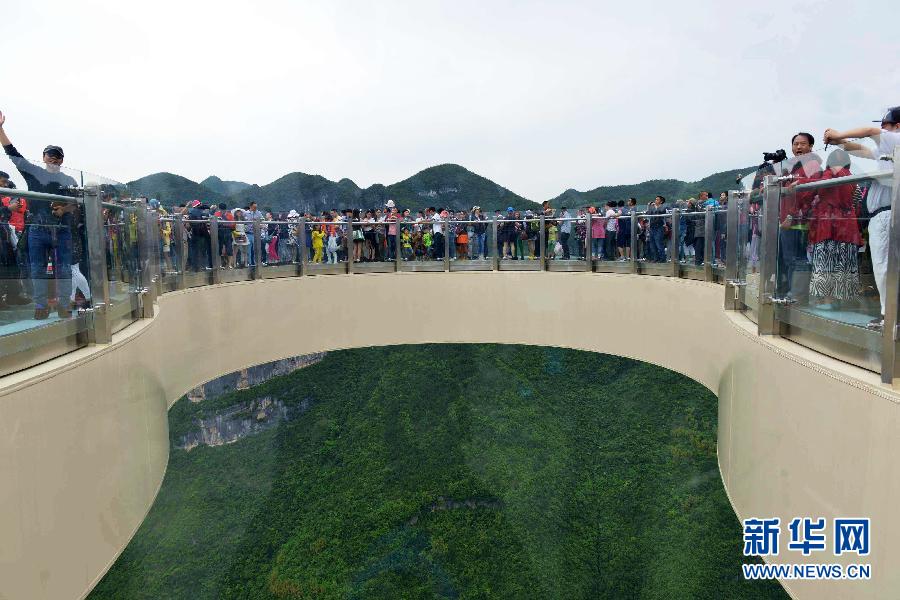 5月3日，游人在重庆市云阳县龙缸景区玻璃廊桥游玩。这座重达900吨的“几”字形玻璃廊桥，如一朵盛开的“空中之花”，悬扣在云阳龙缸景区海拔1010米的绝壁之巅，其中悬挑部分为21.34米，离地高度718米，无钢架支撑，游客站在廊桥上，全景透视脚下的喀斯特地质景观与悬崖绝壁之间的绿树丛荫，独特的视觉画卷尽收眼底。[新华社]