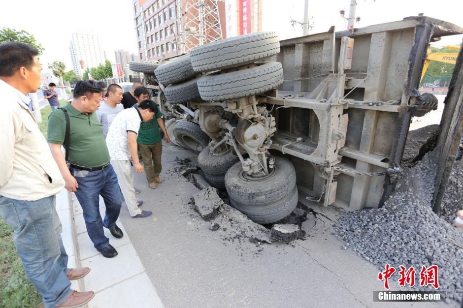 A truck rolls over after falling into a sinkhole on a road in Zhengzhou city in central China's Henan province on May 20, 2015. [Photo: Chinanews.com]