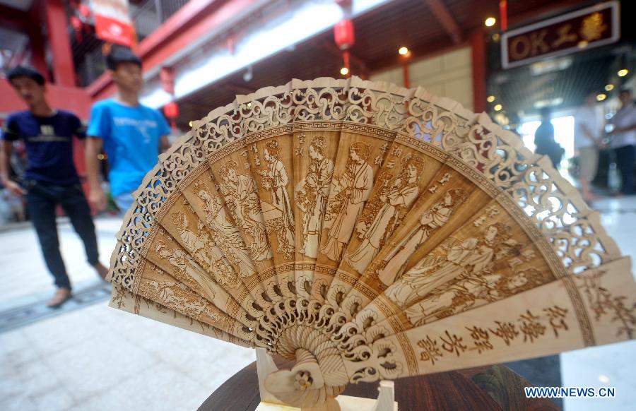 People walk past a wooden fan displayed during a wood art show in Xianyou, southeast China's Fujian Province, June 25, 2015. A wood art show was held in Duwei Township of Xianyou in Fujian Province on Thursday. Duwei Township is home to nearly 1,000 wood carving workshops, and the local expertise in decorative wood carving has a history of almost 1,000 years. [Xinhua]