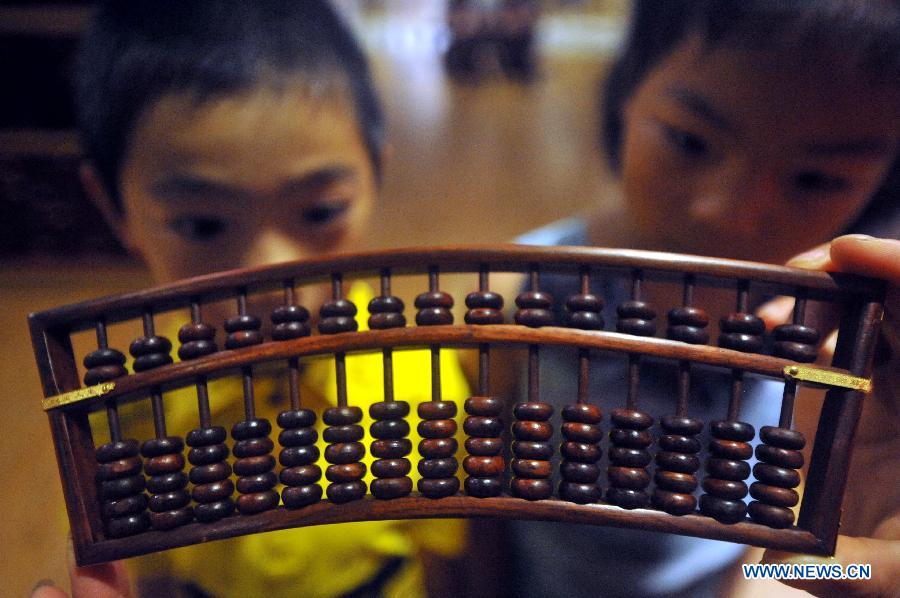 Children look at a wooden abacus displayed during a wood art show in Xianyou, southeast China's Fujian Province, June 25, 2015. A wood art show was held in Duwei Township of Xianyou in Fujian Province on Thursday. Duwei Township is home to nearly 1,000 wood carving workshops, and the local expertise in decorative wood carving has a history of almost 1,000 years. [Xinhua]