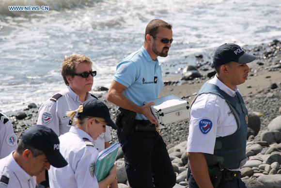 Police officers leave the beach with a container holding metallic debris found on it in Saint-Denis, the Reunion Island, Aug. 2, 2015. A piece of metal was found on a beach near Saint-Denis. The flaperon discovered on Reunion Island has been officially identified as being part of a Boeing 777 aircraft, the same type of plane of the missing flight of Malaysia Airlines MH370. [Photo/Xinhua]