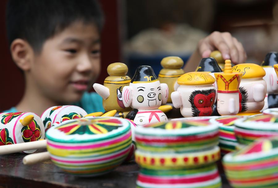  A child in Fannian Village curiously examines a group of wood-cut toys. [Photo/Xinhua]