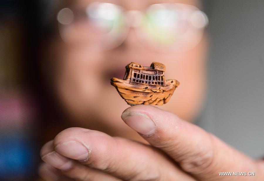 Folk artist Hu Yinsong shows a peach pit carving in Tongxiang, east China's Zhejiang Province, Aug. 26, 2015. Tongxiang has a tradition of wearing peach pit carving for children. [Xinhua]