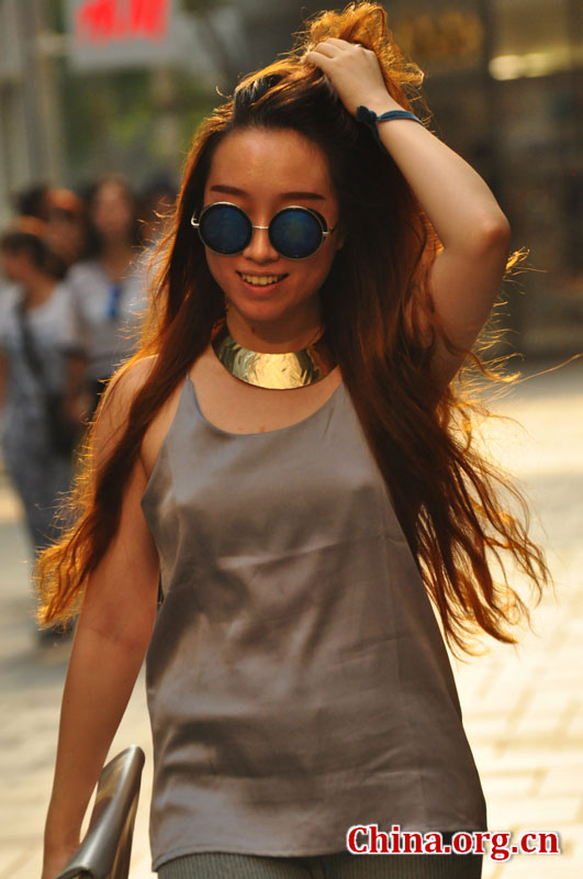 A chic woman wearing a pair of fashionable sunglasses and a huge necklace brushes back her hair while walking through the streets of Sanlitun on Sept. 6, 2015. [Photo by GuoYiming/China.org.cn]