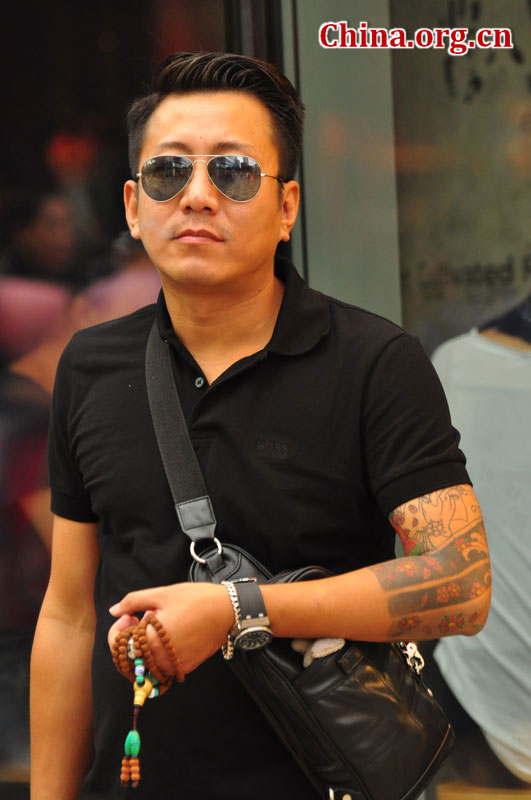 A man wearing a pair of aviator sunglasses holds a Buddha bead necklace on a Sanlitun street on Sept. 6, 2015. [Photo by GuoYiming/China.org.cn]