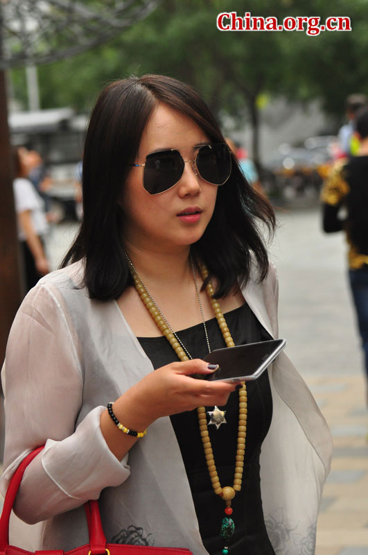 A chic woman wearing a pair of unique aviator sunglasses with a Buddha bead necklace and bracelet walks through the streets of Sanlitun on Sept. 6, 2015. [Photo by GuoYiming/China.org.cn]