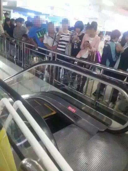 Onlookers taking photos of the broken escalator in a shopping mall in northeast China's city of Shenyang after one section fell off on September 13, 2015. [Photo: Sina.com]