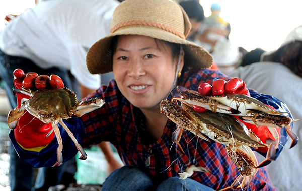 A woman holds three sea crabs at a Lianyungang wharf in Jiangsu province. Sales of seafood products are popular on Chinese e-commerce platforms. [Photo/China Daily]
