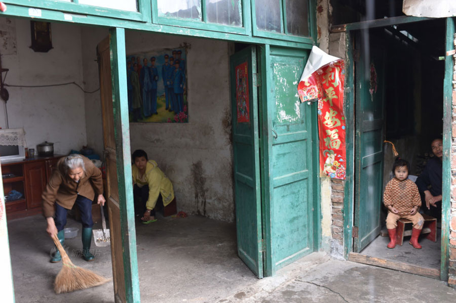 Huang Huiying, 66, lives in Shatang Village, Lingui County in southern China's Guangxi Zhuang Autonomous Region. During the long years, Huang has endured all kinds of hardships, struggling to bring up her three mentally-retarded children and two healthy grandchildren. In the picture, Huang does housework while her children and granddaughter watch. [Photo/Sina]