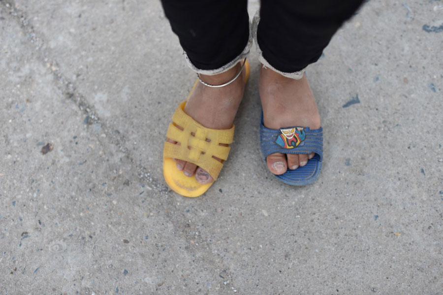 Huang Huiying's second granddaughter wears slippers of different size and color which Huang picked up in a garbage heap. [Photo/Sina] 