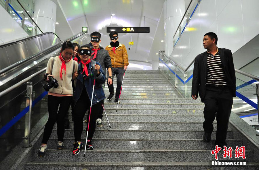 Accompanied by volunteers, a group of college students cover their eyes with eye patches in a bid to understand the challenges faced by blind people when navigating the city's public transportation system. The experiment took place at a subway station in Kunming, the capital of southwest China's Yunnan province on October 15, 2015. These are part of the activities to mark the International Blind Day. [Chinanews.com]