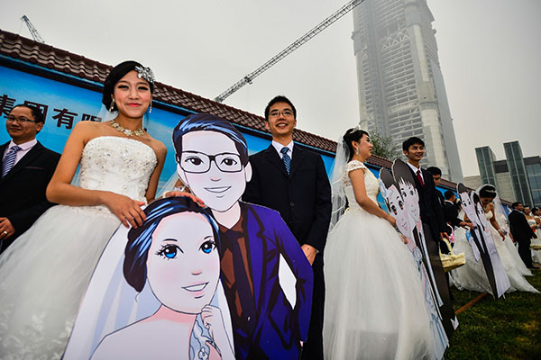 A couple poses for a photo with their cartoon-image poster at the group wedding in Tianjin on Oct 20, 2014. [Photo/Xinhua] 