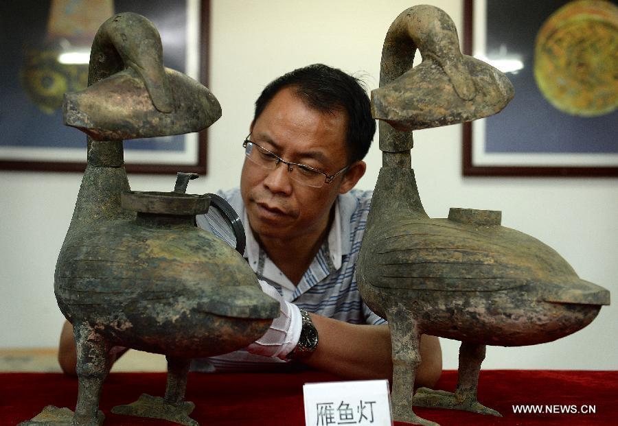 Photo taken on Aug. 6, 2015 shows an archaeologist studying on the bronze lamps unearthed from the excavation site of royal tombs of Marquis of Haihun State during the West Han Dynasty (206 B.C.--25 A.D.) in Nanchang, capital of east China's Jiangxi Province.[Photo/Xinhua]