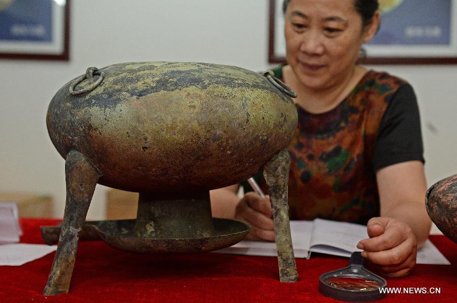 Photo taken on Aug. 6, 2015 shows an archaeologist studying on a bronze pot unearthed from the excavation site of royal tombs of Marquis of Haihun State during the West Han Dynasty (206 B.C.--25 A.D.) in Nanchang, capital of east China's Jiangxi Province.[Photo/Xinhua]