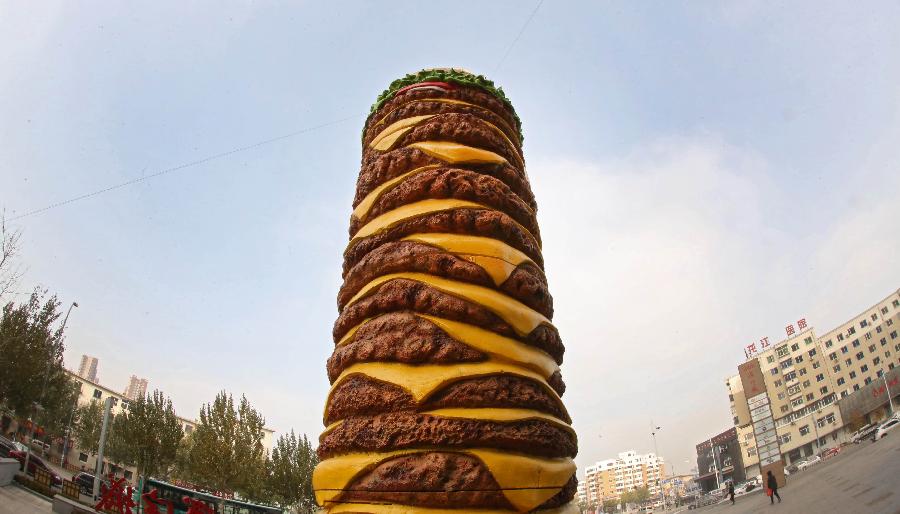 A huge hamburger model is seen near a shopping mall in Shenyang, capital of northeast China's Liaoning Province on Nov. 11, 2015. The 2-tonne hamburger model is 10 meters in height and 2.5 meters in diameter. [Xinhua]