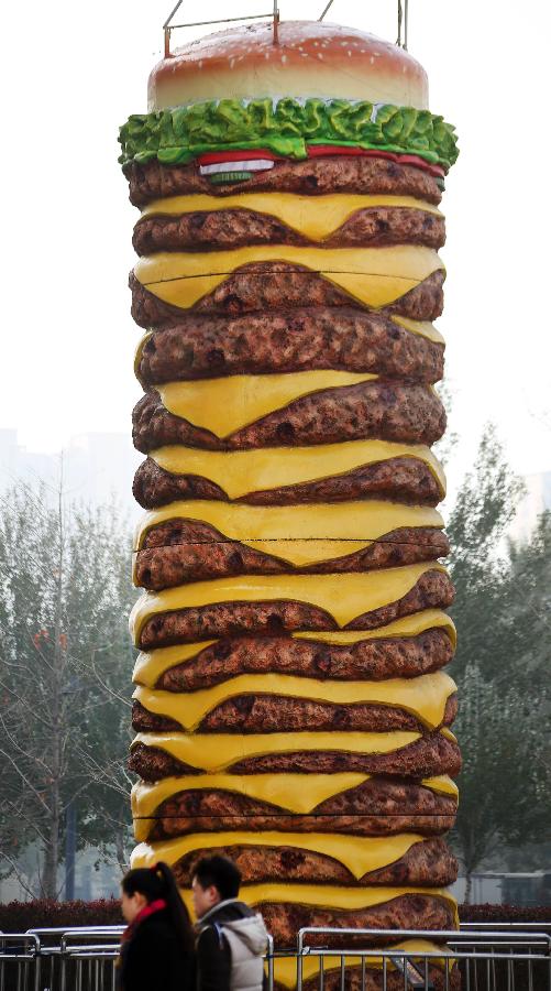 A huge hamburger model is seen near a shopping mall in Shenyang, capital of northeast China's Liaoning Province on Nov. 11, 2015. The 2-tonne hamburger model is 10 meters in height and 2.5 meters in diameter. [Xinhua]