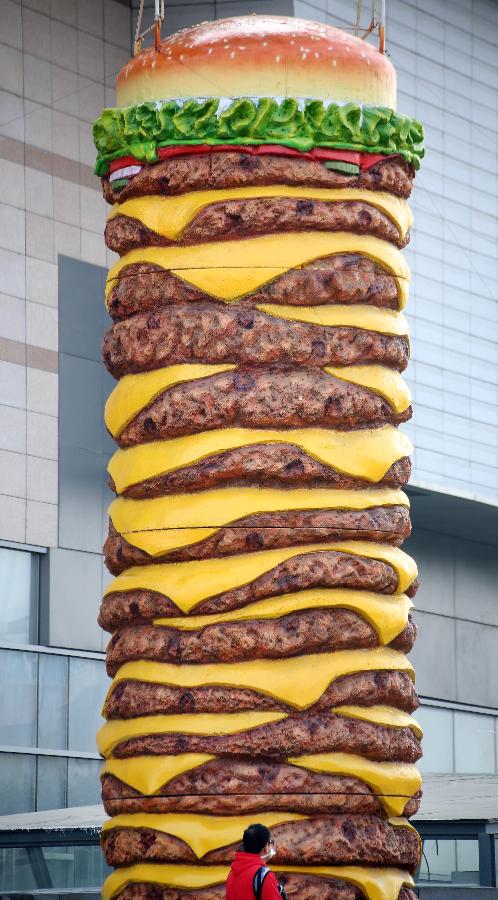 A huge hamburger model is seen near a shopping mall in Shenyang, capital of northeast China's Liaoning Province on Nov. 11, 2015. The 2-tonne hamburger model is 10 meters in height and 2.5 meters in diameter. [Xinhua]