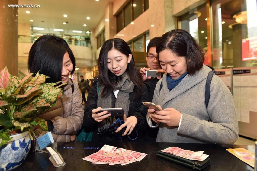 Reporters take photos of new 100-yuan banknotes at the Beijing Branch of the Bank of Communication in Beijing, capital of China, Nov. 12, 2015. China's central bank released a new 100-yuan banknote on Thursday. The design stays largely the same as its former series, but the new banknotes are harder to conterfeit and easier for machines to read. The 100-yuan note is the largest denomination of the Chinese currency. [Xinhua]