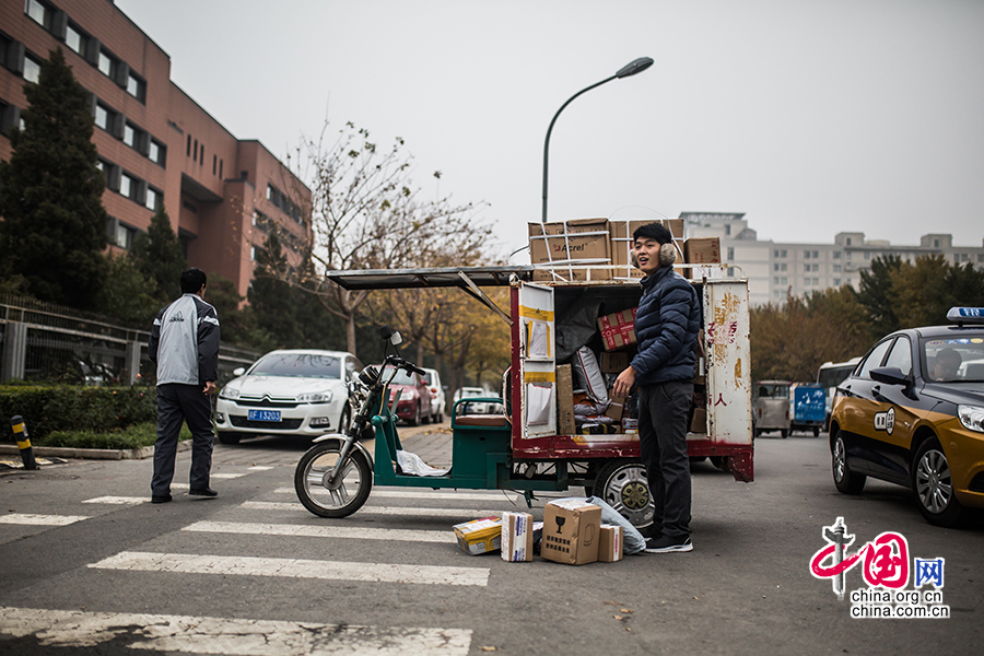 Hou arrives at his first destination of the day. As he is not allowed to enter the building, he has to park his electric motorcycle at the roadside and contact the customer on his cell phone. [Photo by Zheng Liang/China.org.cn]