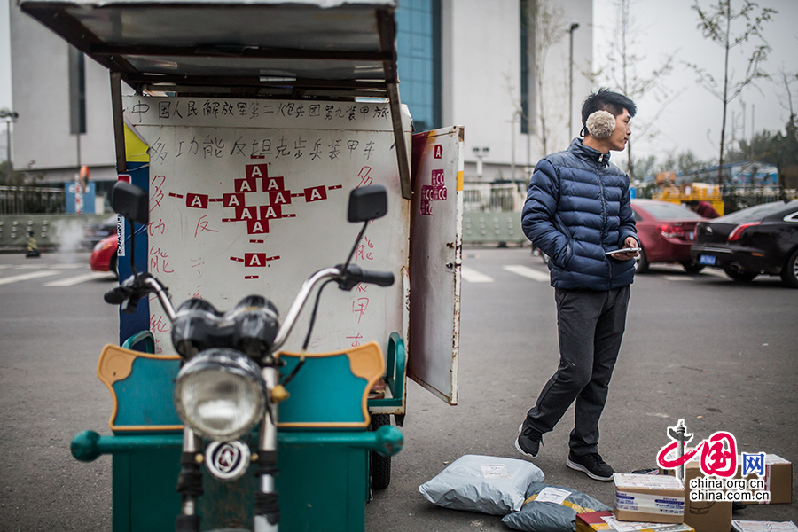 Hou parks his electric motorcycle at the roadside and contacts his customers by cell phone. On the motorcycle are the Chinese characters 'multi-functional anti-tank infantry armored vehicle' written by Hou for fun. [Photo by Zheng Liang/China.org.cn]