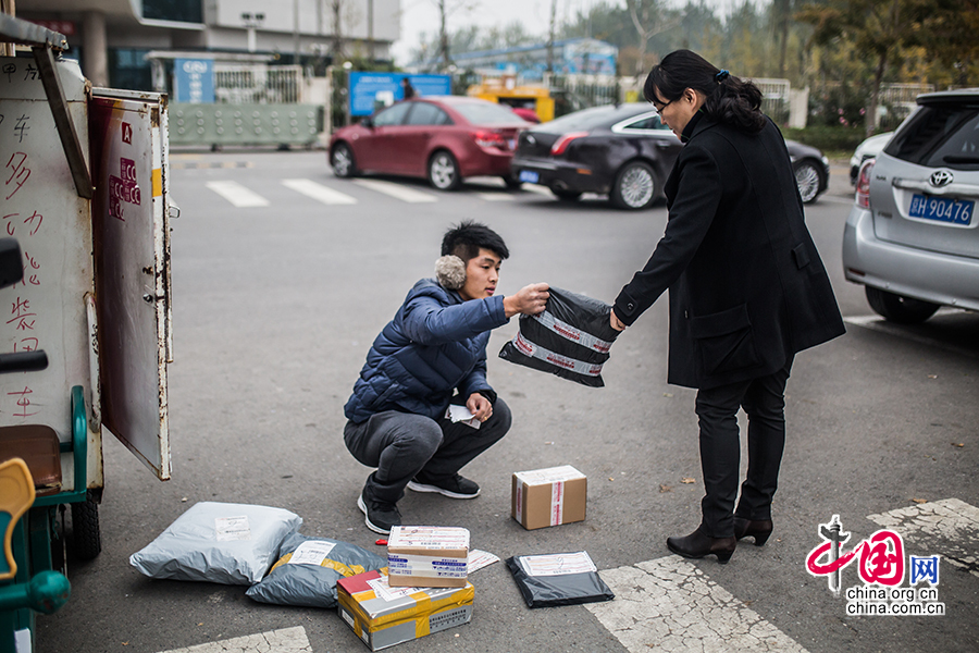 Hou arrives at his first destination of the day. As he is not allowed to enter the building, he has to park his electric motorcycle at the roadside and contact the customer by cell phone. A woman comes out to collect her package. [Photo by Zheng Liang/China.org.cn]