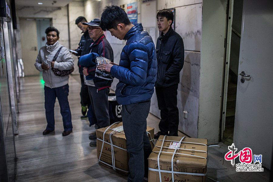 Hou examines the dispatch list while waiting for an elevator with two large packages by his side. [Photo by Zheng Liang/China.org.cn]