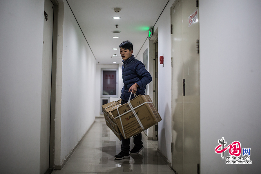 Hou carries two large packages and waits for an elevator. [Photo by Zheng Liang/China.org.cn]