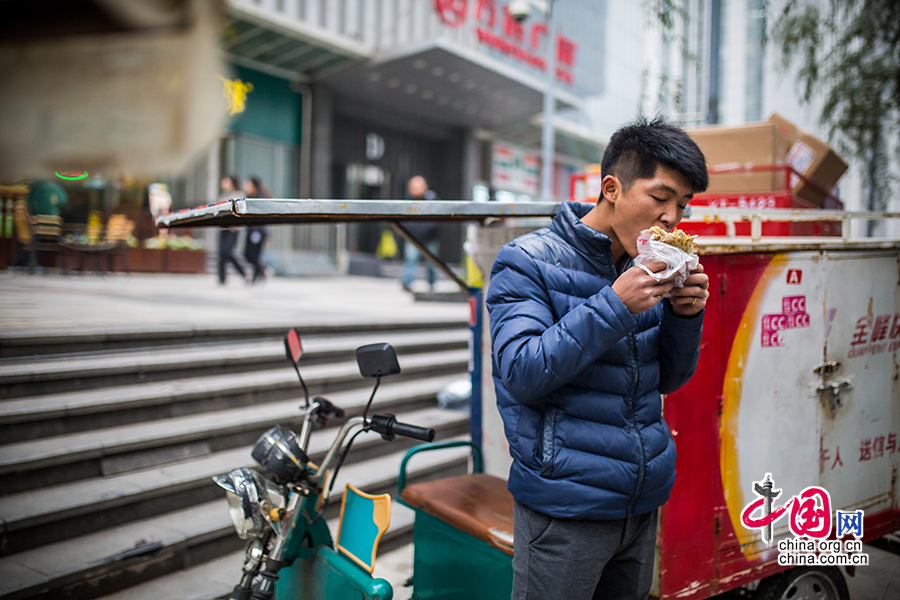 Hou eats a simple meal between deliveries. The meal is usually a fried pancake rolled with egg filling and washed down with a bottle of mineral water. [Photo by Zheng Liang/China.org.cn]