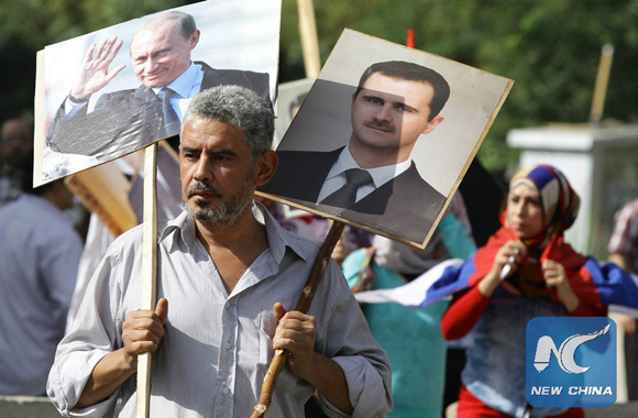 A Syrian man holding up portraits of President Bashar al-Assad and his Russian counterpart Valdimir Putin (L) joins several hundred people who gathered near the Russian embassy in Damascus on October 13, 2015 to express their support for Moscow's air war in Syria. [Photo/Xinhua]