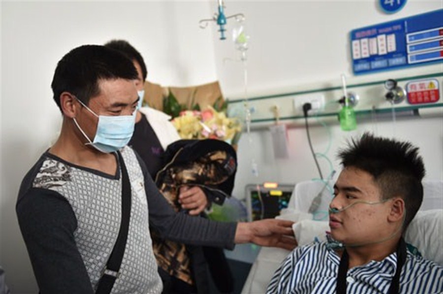 At a hospital in Shenzhen yesterday, Tian Zuming (left) visits his son Tian Zeming, who was pulled out alive almost 72 hours after a landslide buried dozens of buildings in the city.[Photo/Xinhua]