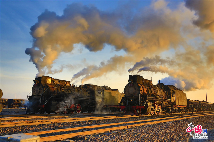 Steam trains cross an opencast coal mine at Sandaoling in Hami prefecture, Northwest China's Xinjiang Uygur Autonomous Region, Jan 13, 2016. Six steam trains are still used at Sandaoling, however, they will be gradually replaced by new electric engines this year. Three people - an engineer, an assistant engineer and a stoker - are needed to operate the trains. The designed speed is 70 km per hour, but they run at 20 km per hour, and the annual traffic volume is 8 million tons. [Photo/China.org.cn]