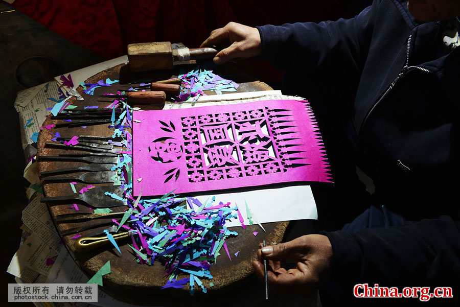 Villager Shi Longjiang makes Guomenjian at his home in Yanzhuang Town, Juxian County of Shandong Province, on Jan. 7, 2016. Guomenjian are red or colorful paper cuts, with auspicious signs and characters, pasted by Chinese people over the doors or windows of their homes to welcome the traditional festivals like the Chinese New Year. [Photo by Chen Weifeng/photostock.china.com.cn]