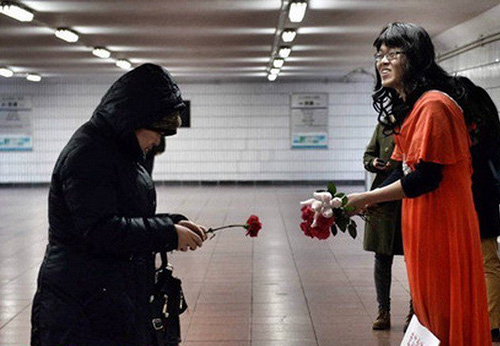 Wearing a thin red robe and a woman's wig, Dong Dajun (Right) tries to attract the attention of pedestrians walking through an underground passage near a Beijing hospital on Jan 13, 2015. [Photo/Beijing Times]