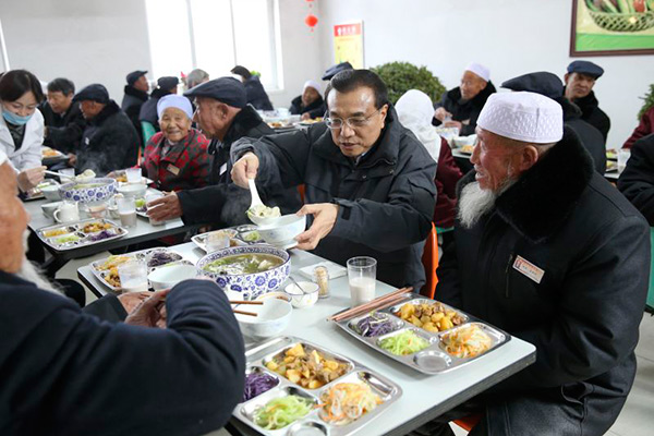 Premier Li fills a bowl of hot dumplings for a senior citizen.[Photo/English.gov.cn] 