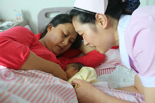 A nurse at a hospital in Xiangyang, Hubei province, helps Chen Jing to breast-feed her second child on Friday. [Photo by Gong Bo/China Daily] 