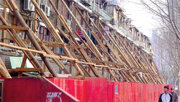 A man walks past an apartment building in Huangpu District, which appears to be supported by wooden struts. [Shanghai Daily]