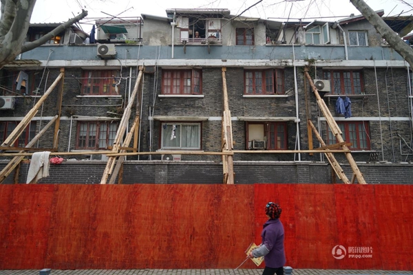 A man walks past an apartment building in Huangpu District, which appears to be supported by wooden struts. [Shanghai Daily]