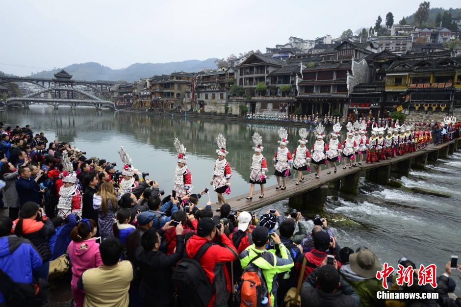 A crowd of tourists take photos of some Miao ethnic women in their local costumes. More than 100 Miao ethnic women gathered in the ancient town of Fenghuang to participate in the 5th China Fenghuang Miao Ethnic Silver-wear and Costumes Festival to showcase their dressings on December 2nd, 2015. [Photo: Chinanews.com]