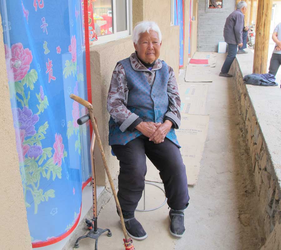 A woman sits in front of a newly built nursing home. The home houses local solitary elders. [Photo by Wu Yan/chinadaily.com.cn]