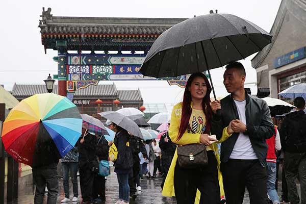 Tourists visit Nanluoguxiang as drizzle falls in Beijing on Monday.[Photo by Wang Zhuangfei/China Daily]