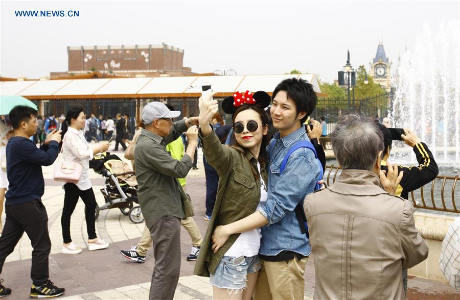 Tourists pose for a selfie outside the Disney Resort in Shanghai, May 7, 2016. Two shops in the Disney Town opened here on Saturday, when the Shanghai Disneyland, Disney's first theme park in the Chinese mainland, started an operational test. [Xinhua] 