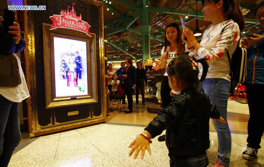 A girl poses in front of an electronic dressing mirror in the Disney Town of the Disney Resort in Shanghai, May 7, 2016. Two shops in the Disney Town opened here on Saturday, when the Shanghai Disneyland, Disney's first theme park in the Chinese mainland, started an operational test. [Xinhua] 