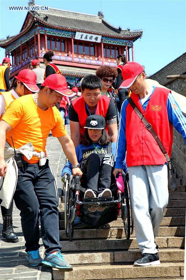 Volunteers help a disabled woman to visit Laolongtou scenic spot in Qinhuangdao, north China's Hebei Province, on May 15, 2016, the National Day for Helping the Disabled, which is marked on the third Sunday of May every year. [Photo/Xinhua]