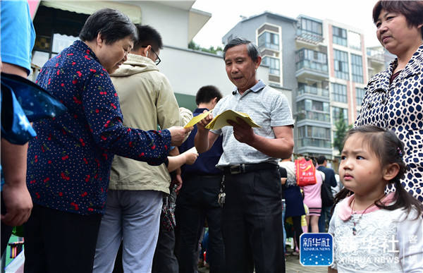 A kindergarten worker issues numbered tickets to parents queuing outside a private kindergarten in Hefei City, Anhui Province on June 6. [Photo by Xinhua News Agency] 